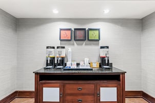 Uma estação de café com dois distribuidores de café, um refrigerador de água e uma bandeja pequena com copos e utensílios.