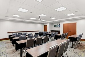 Une salle de conférence équipée de plusieurs tables et chaises, d’un projecteur et d’une porte.