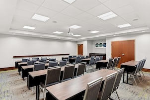 Sala de conferências com várias mesas, cadeiras, um projetor e uma porta.
