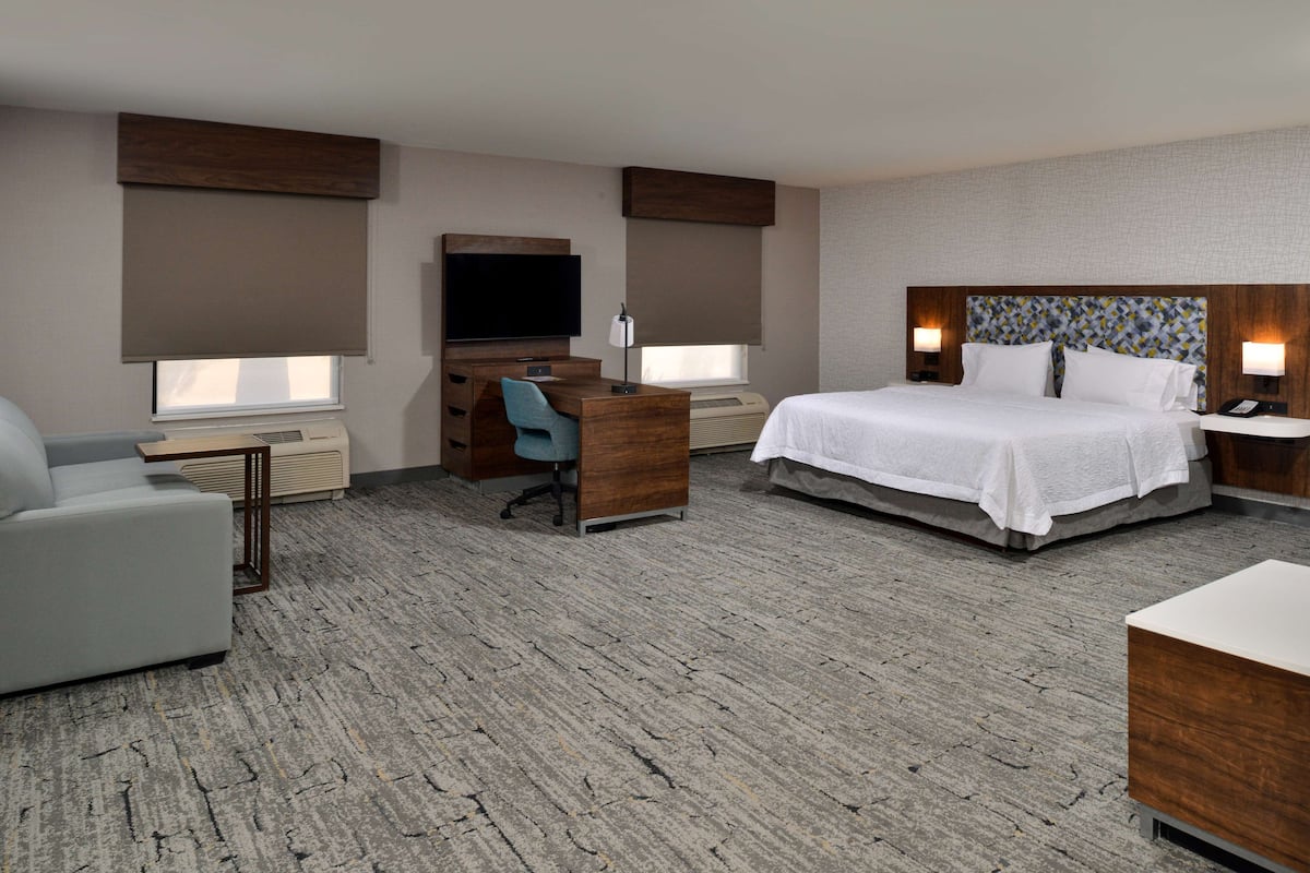 A hotel room with a bed, a desk, a chair, a TV, and a sofa.