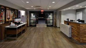 A hotel reception area with a wooden reception desk, a coffee station, and a glass door entrance. - Hampton Inn & Suites Las Vegas Airport (Las Vegas)