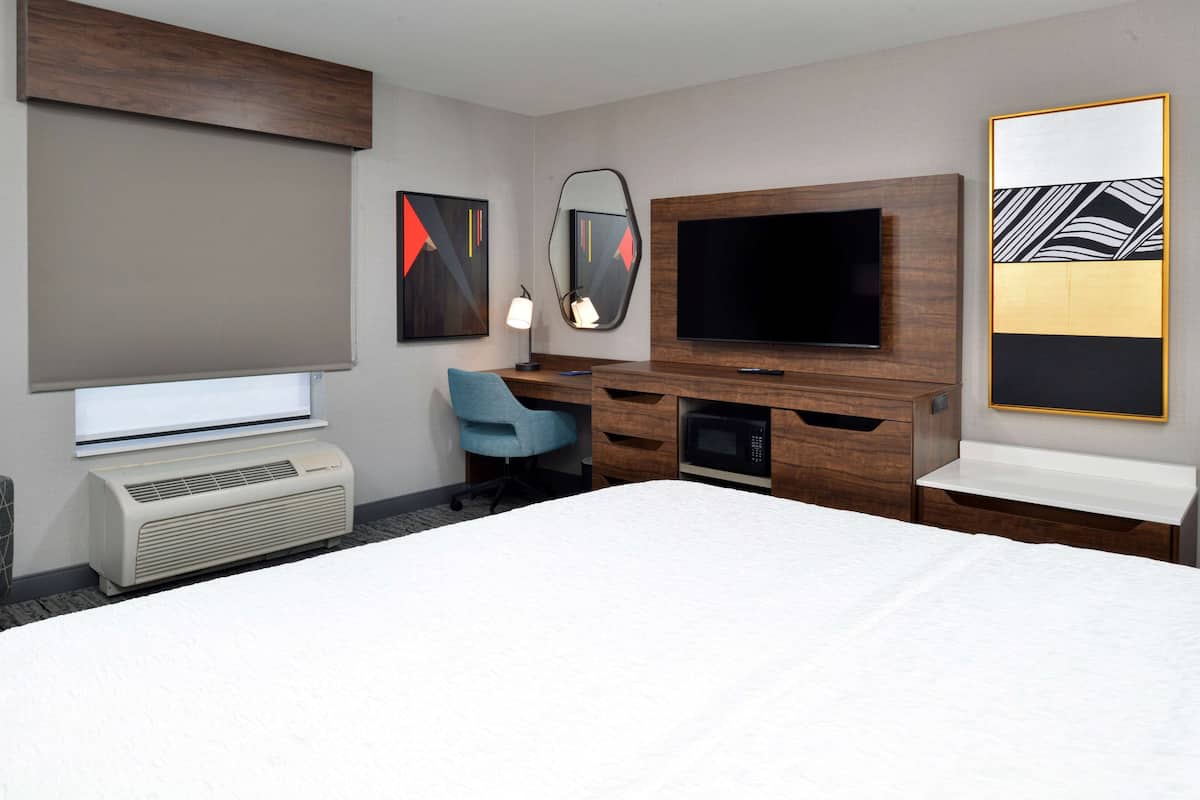 A hotel room with a large bed, a desk with a chair, a flat-screen TV, a microwave, and a large mirror.