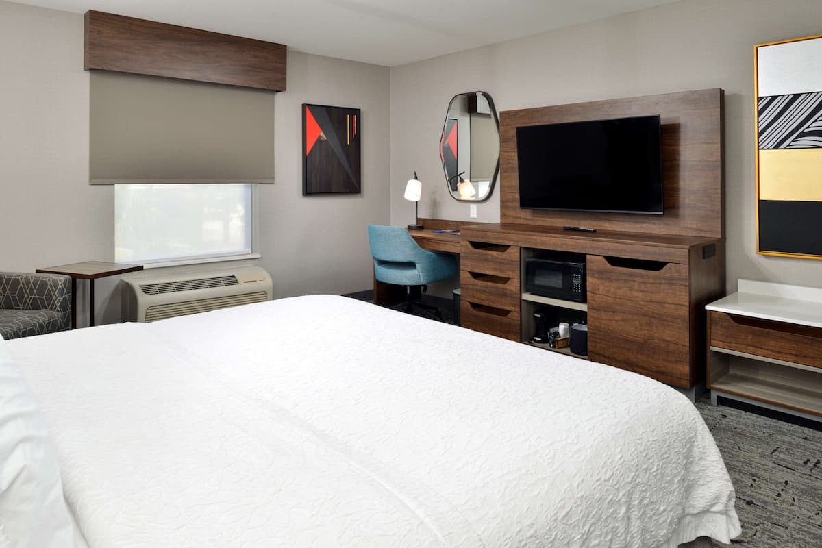 A hotel room with a large bed, a desk with a computer, a TV, and a window with blinds.