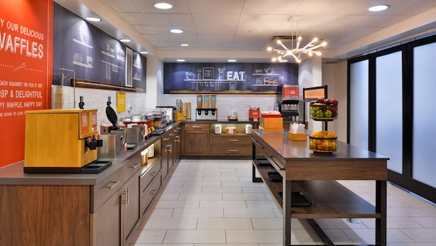 A modern kitchen with a waffle station, a coffee bar, and a fruit display. - Hampton Inn & Suites Las Vegas Airport (Las Vegas)