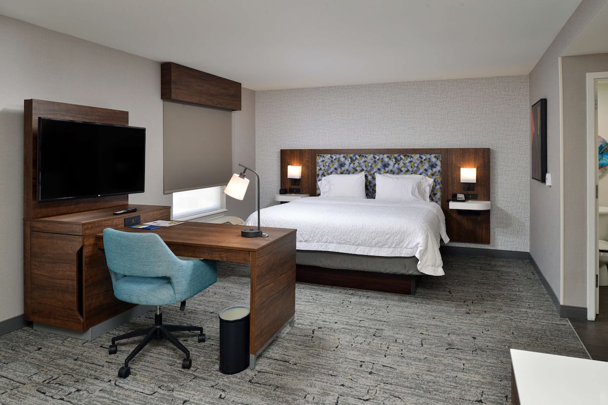 A hotel room with a bed, a desk with a chair, a television, and two bedside lamps.