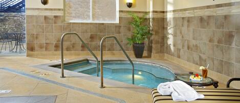 A spa area with a hot tub, a lounge chair, and a small table with a drink and fruit.