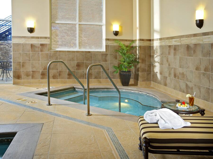 Un espace spa comprenant un bain à remous, une chaise longue et une petite table avec une boisson et des fruits.