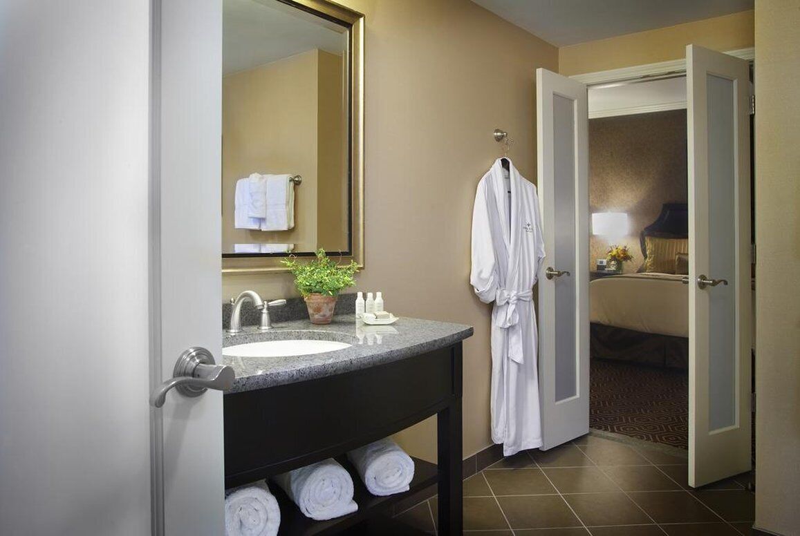 A hotel bathroom with a sink, mirror, towels, and a robe hanging on the wall.