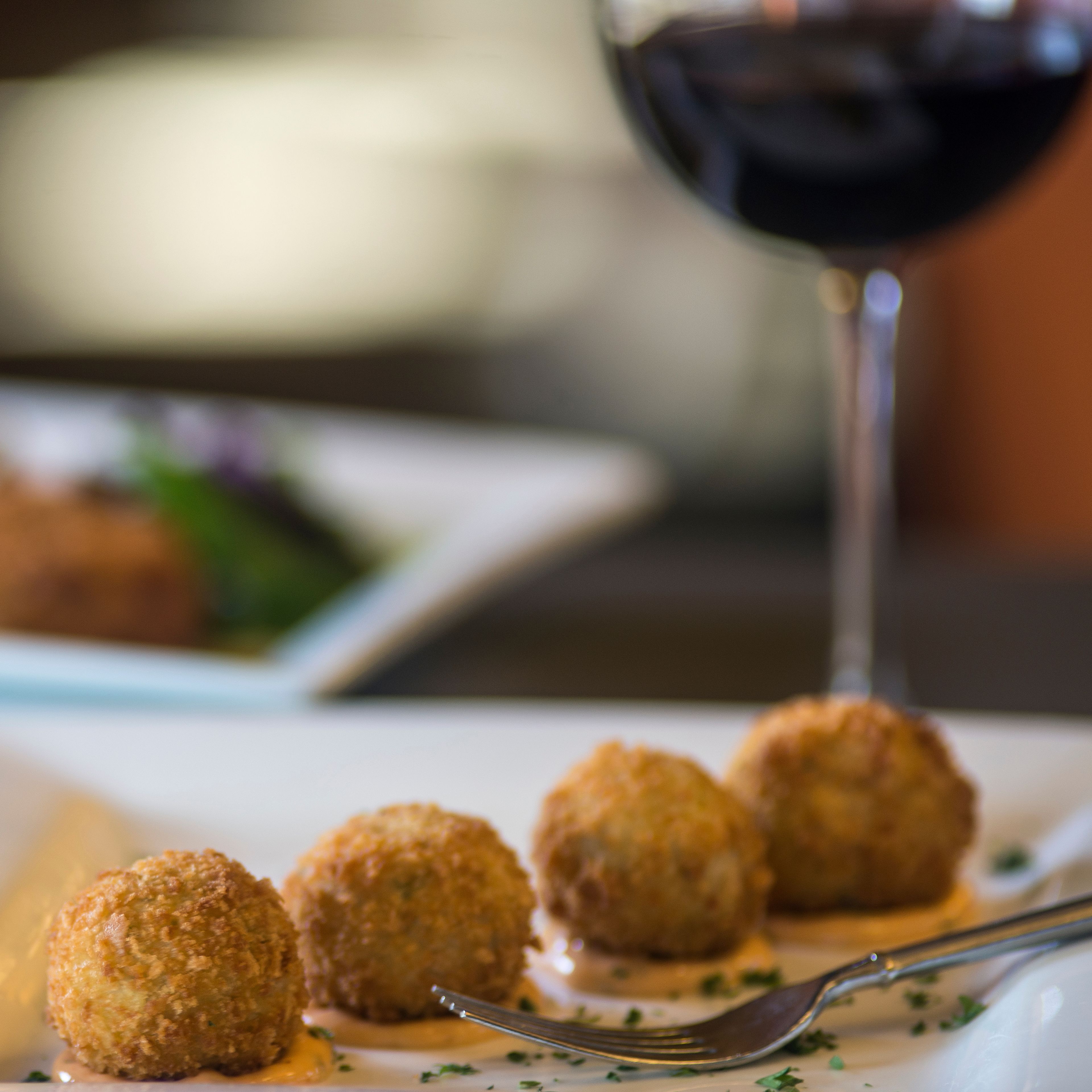 Un plato de croquetas y una copa de vino tinto.