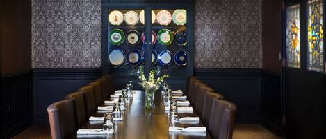 A formal dining room with a long table, multiple chairs, a vase with flowers, and a wall display of plates.
