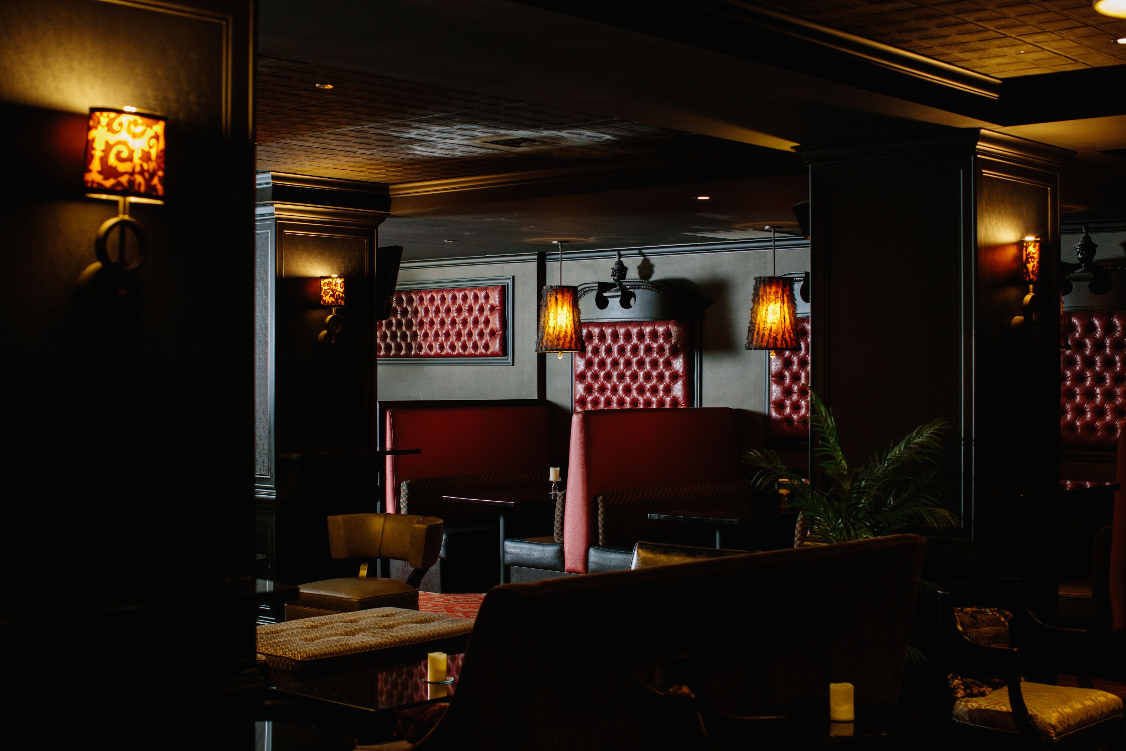 Un intérieur à la lumière tamisée, avec des sièges recouverts d ’un tissu rouge, des panneaux muraux à motifs et des lampes fixées au mur.