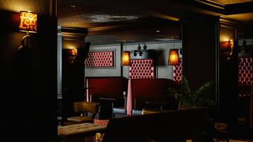 A dimly lit interior with red upholstered seating, patterned wall panels, and wall-mounted lamps.