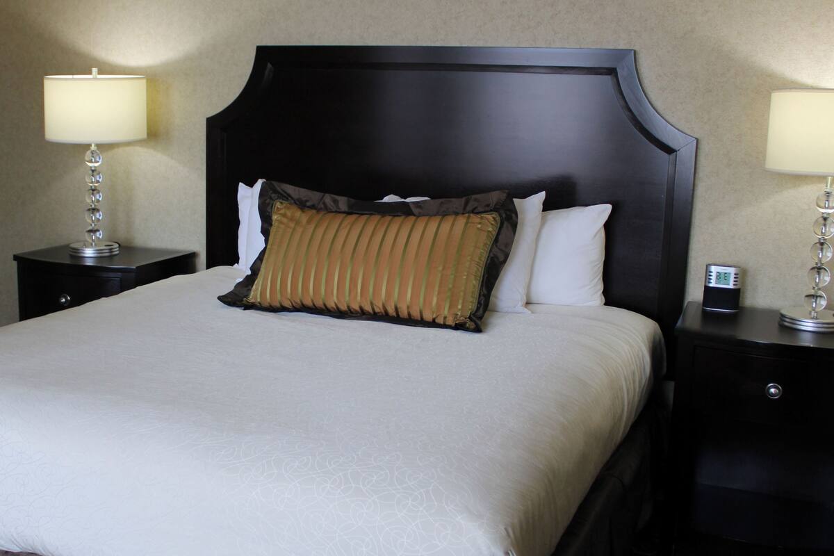 A neatly made bed with a large headboard, two bedside tables with lamps, and a digital clock on one of the tables.