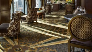 Un lobby espacioso con alfombra estampada, techo ornamentado y mobiliario clásico.