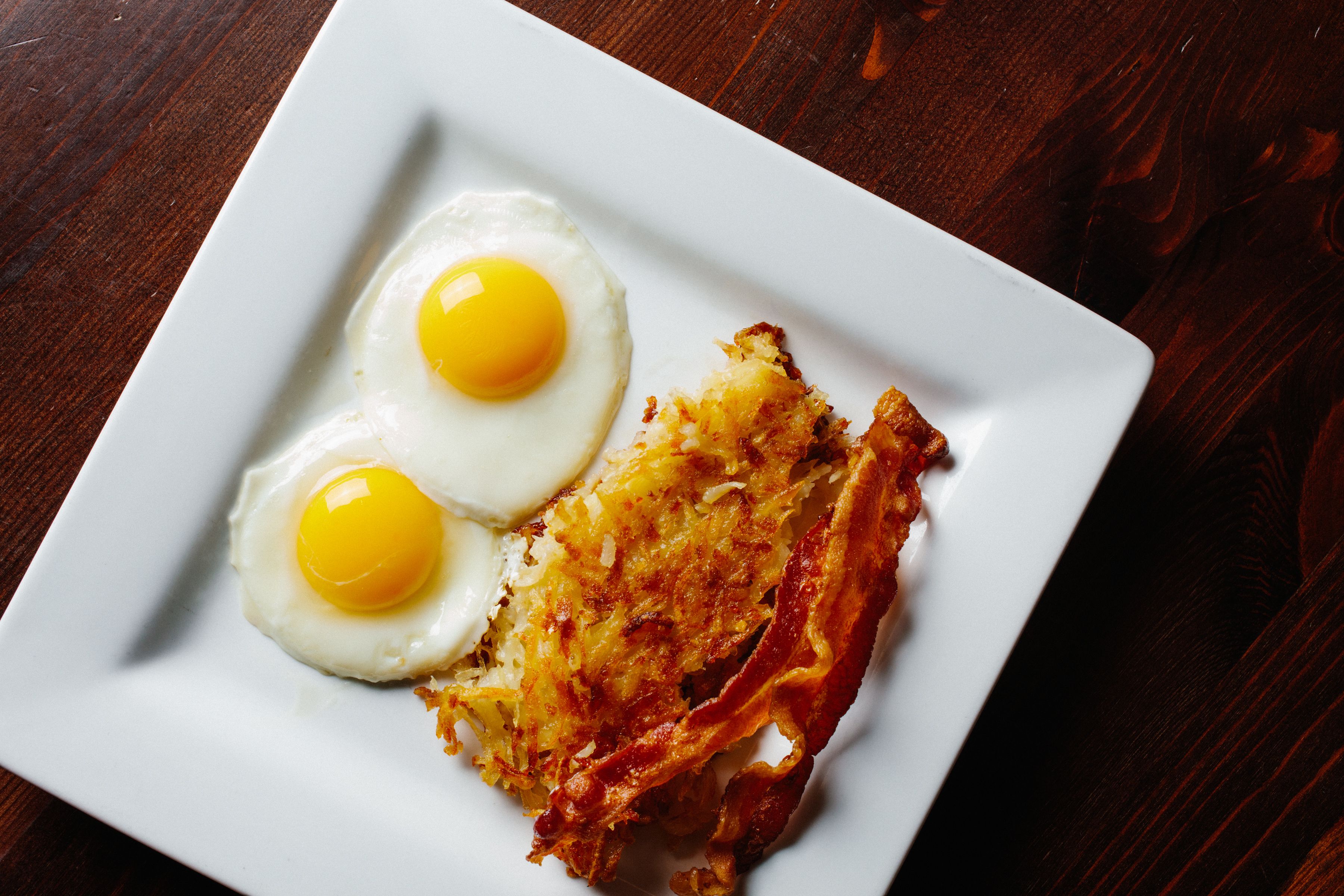 A white plate with two sunny-side-up eggs and a hash brown.