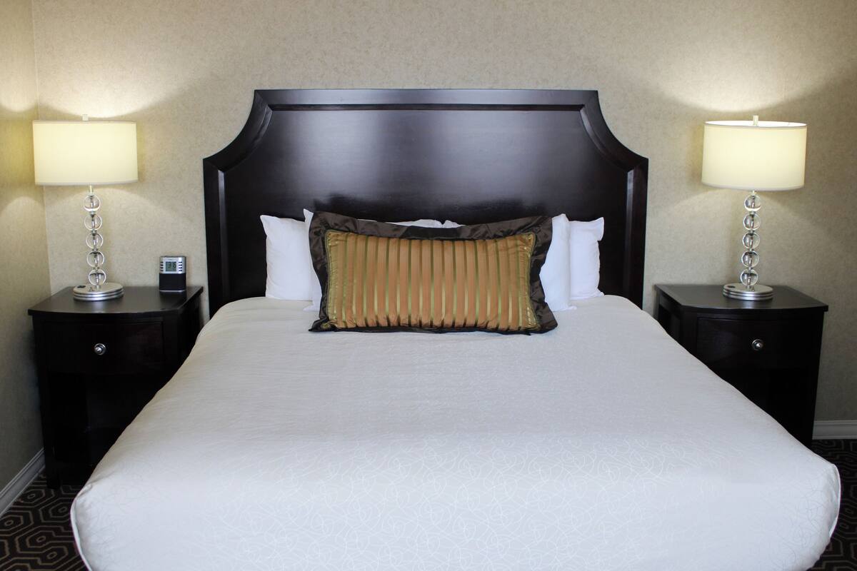 A hotel room with a large bed, two bedside tables with lamps, a digital clock, and a patterned carpet.