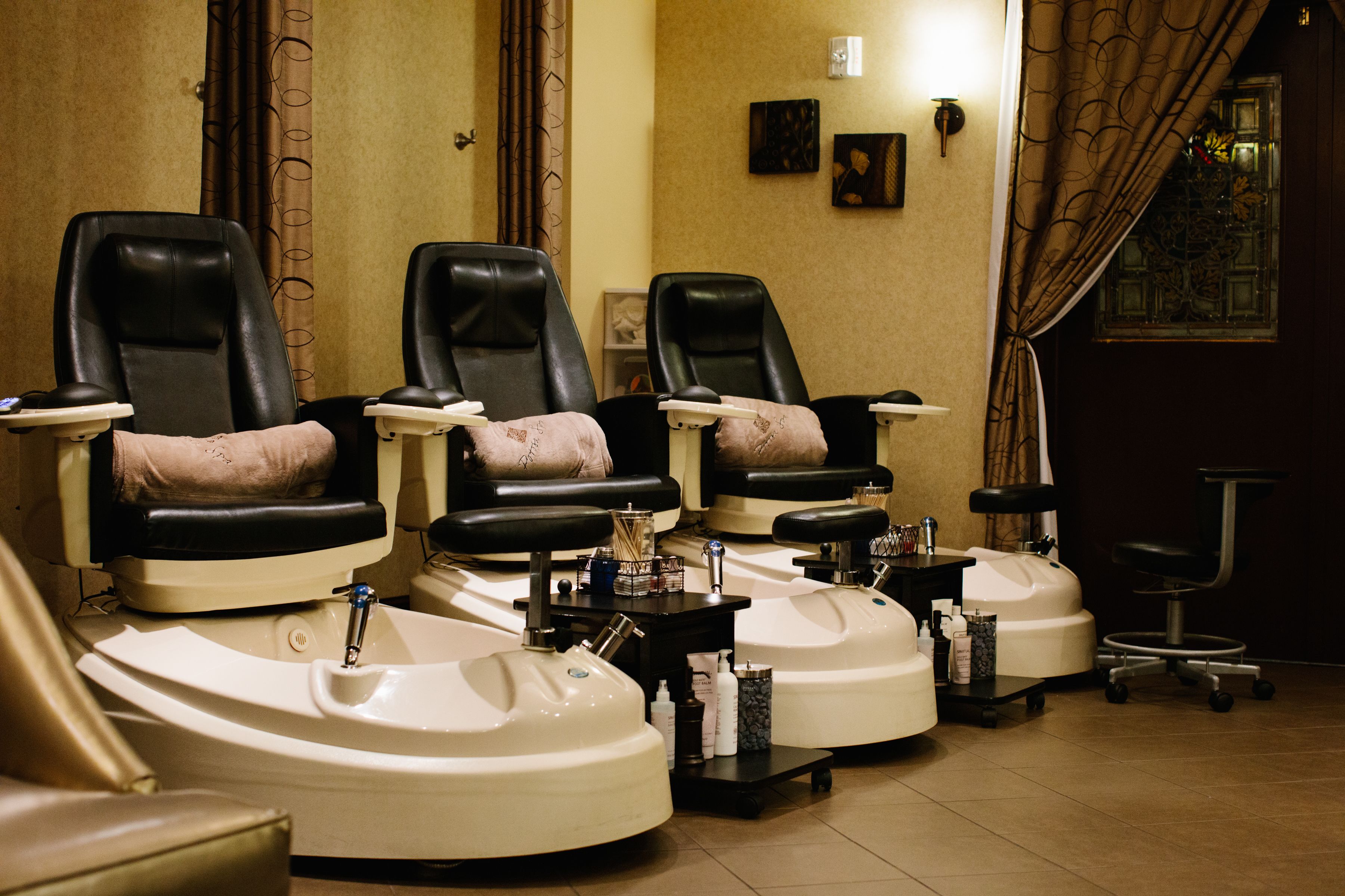 Un salon équipé de trois fauteuils et de trois bacs à shampoing, d’une petite table où sont rangés les produits, et d’une fenêtre avec des rideaux.