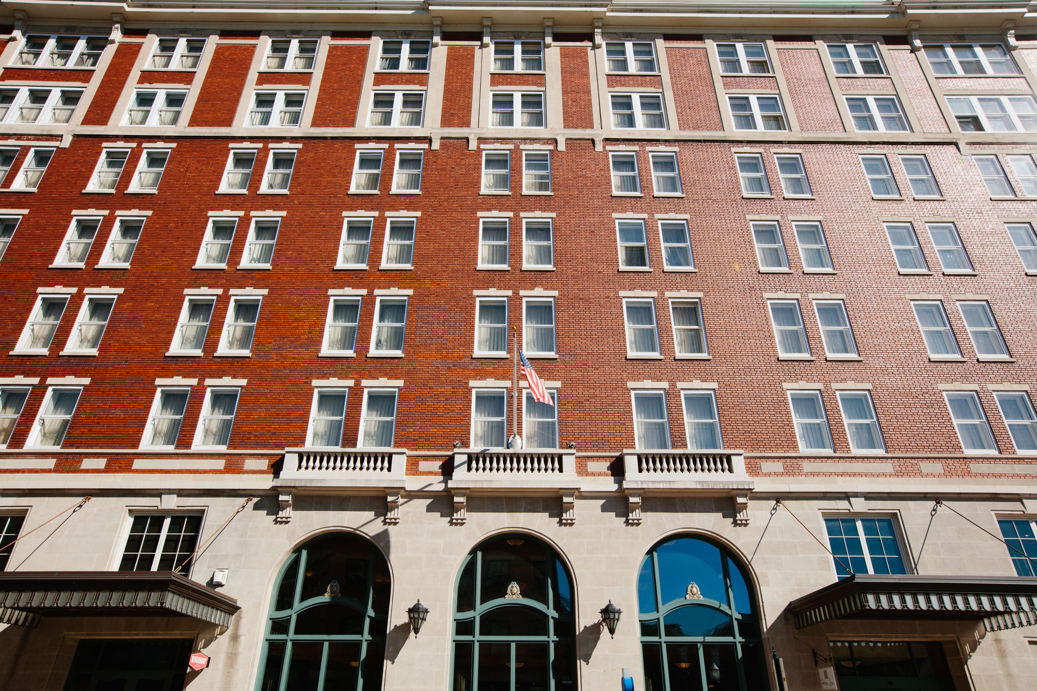 A multi-story building with a red brick facade, multiple windows, and a flag.