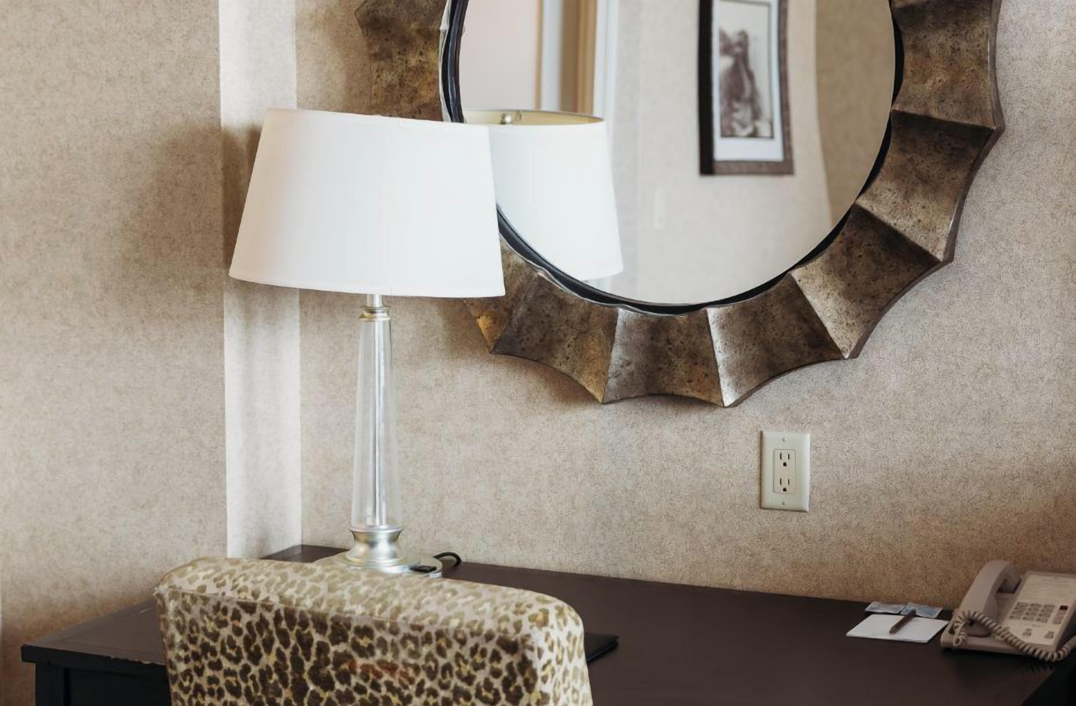 A hotel room with a lamp on a table, a telephone, and a mirror on the wall.