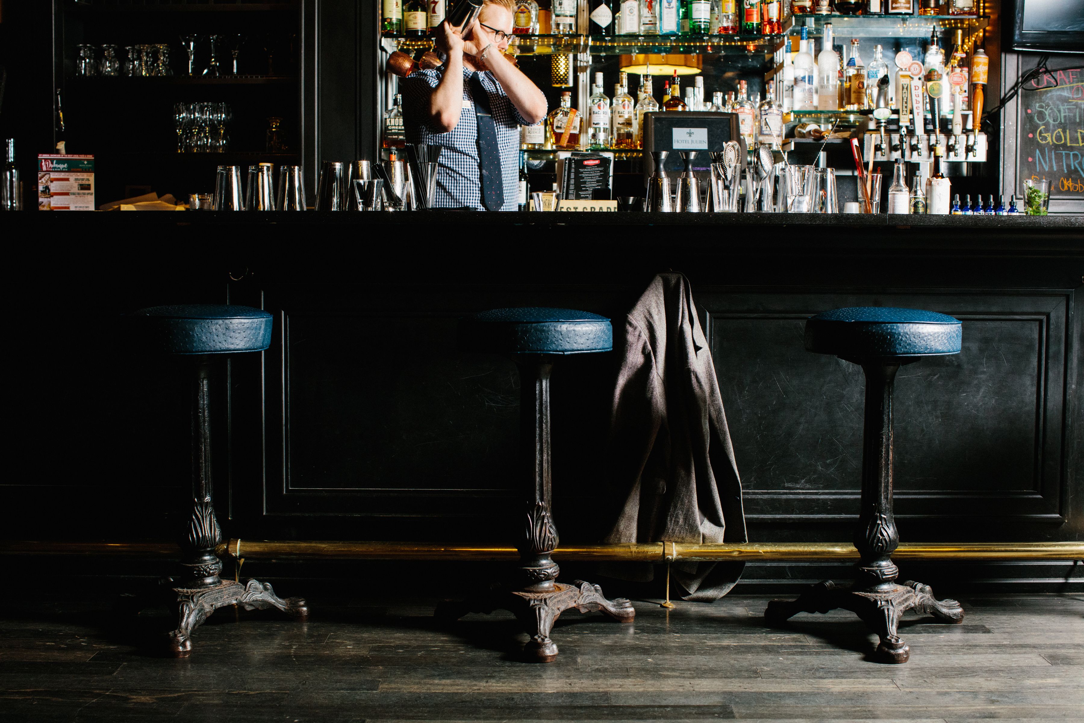 Uma área de bar com banquetas, balcão e diversos tipos de garrafas e copos.