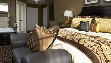 A hotel room with a large bed, a chair, a desk with a lamp, and a framed picture on the wall.