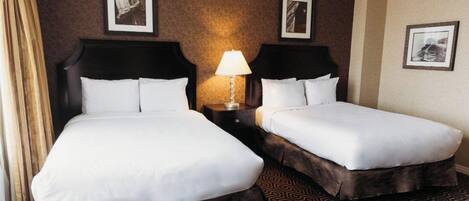 Habitación de hotel con dos camas, una mesita de noche con lámpara y alfombra estampada.