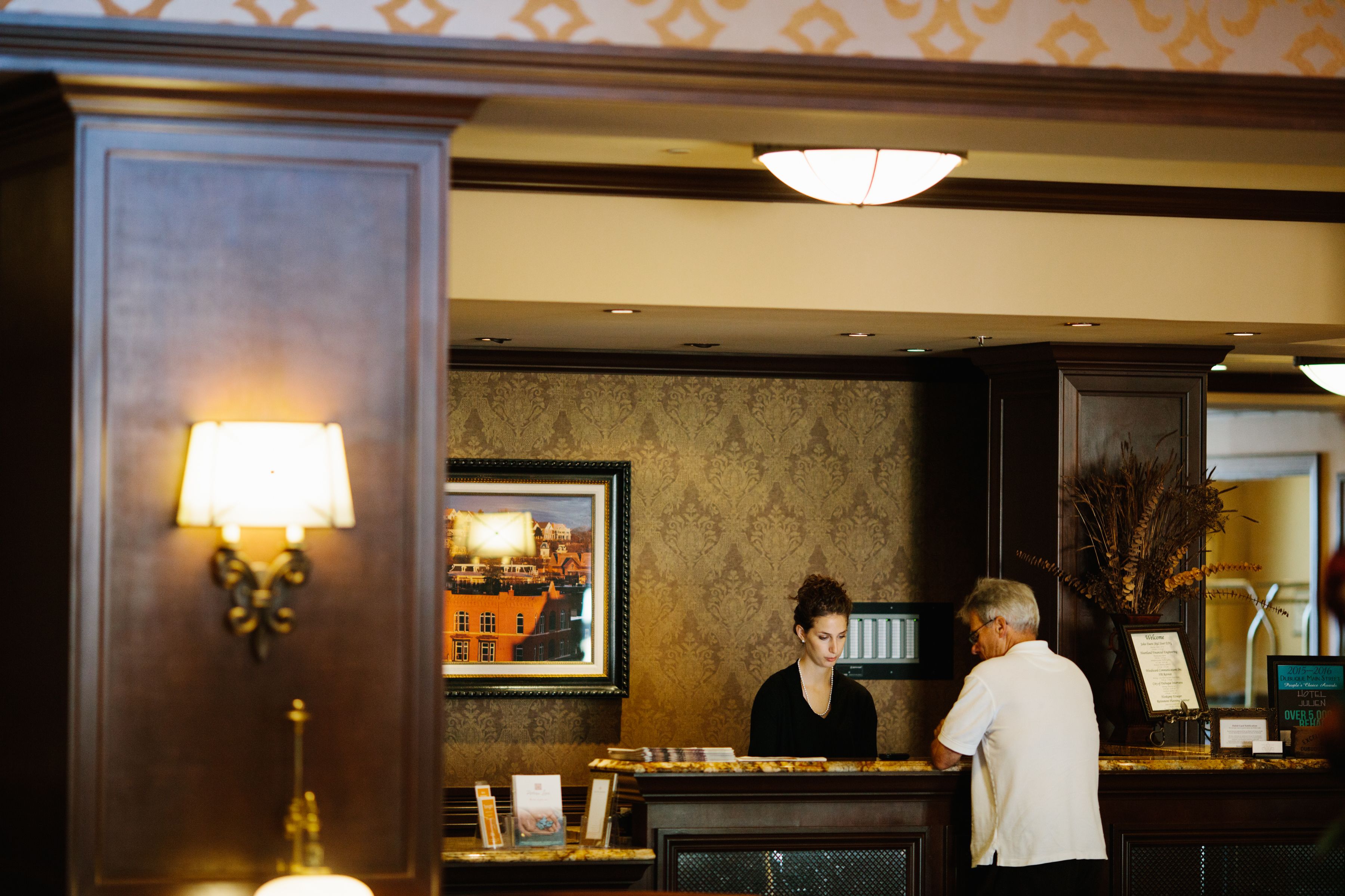 A reception area with a wooden reception desk, a framed cityscape painting, and a wall-mounted lamp.