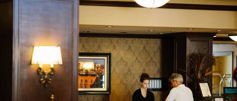 A reception area with a wooden reception desk, a framed cityscape painting, and a wall-mounted lamp.