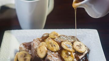 A plate of bread pudding topped with bananas and syrup, with a cup of coffee in the background.