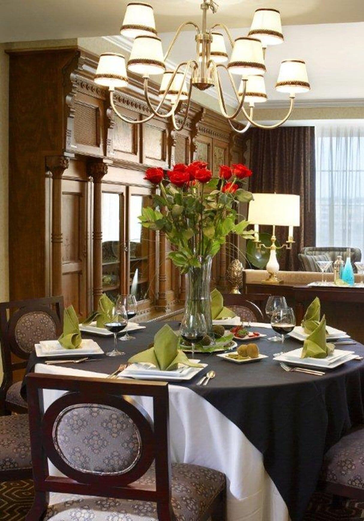 A formal dining room with a chandelier, a vase of red roses, and neatly set tables.