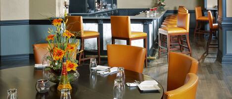 A dining area with a round table, orange chairs, a vase with flowers, and a hanging lamp.