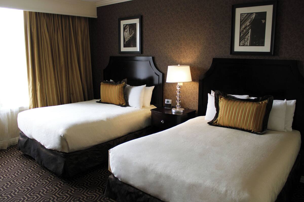 A hotel room with two beds, a nightstand with a lamp, and framed pictures on the wall.
