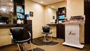 Een kapsalon met twee zwarte stoelen, een balie met diverse producten en een presentatie voor Sorme Treatment & Cosmetics.