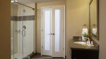 A bathroom with a glass shower enclosure, a white door, a sink with a mirror, and a towel rack.