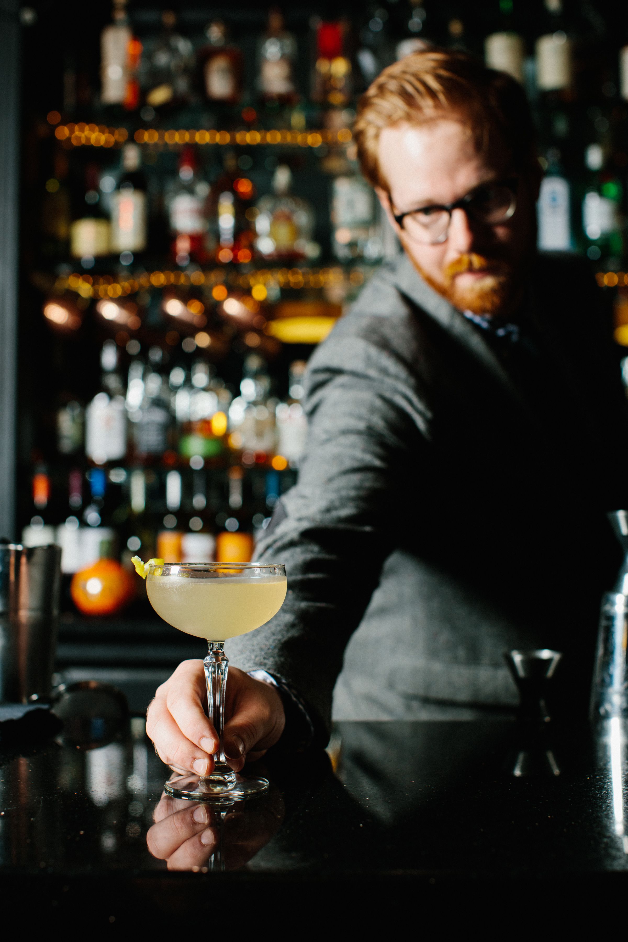 A bar setting with a bartender holding a cocktail glass.