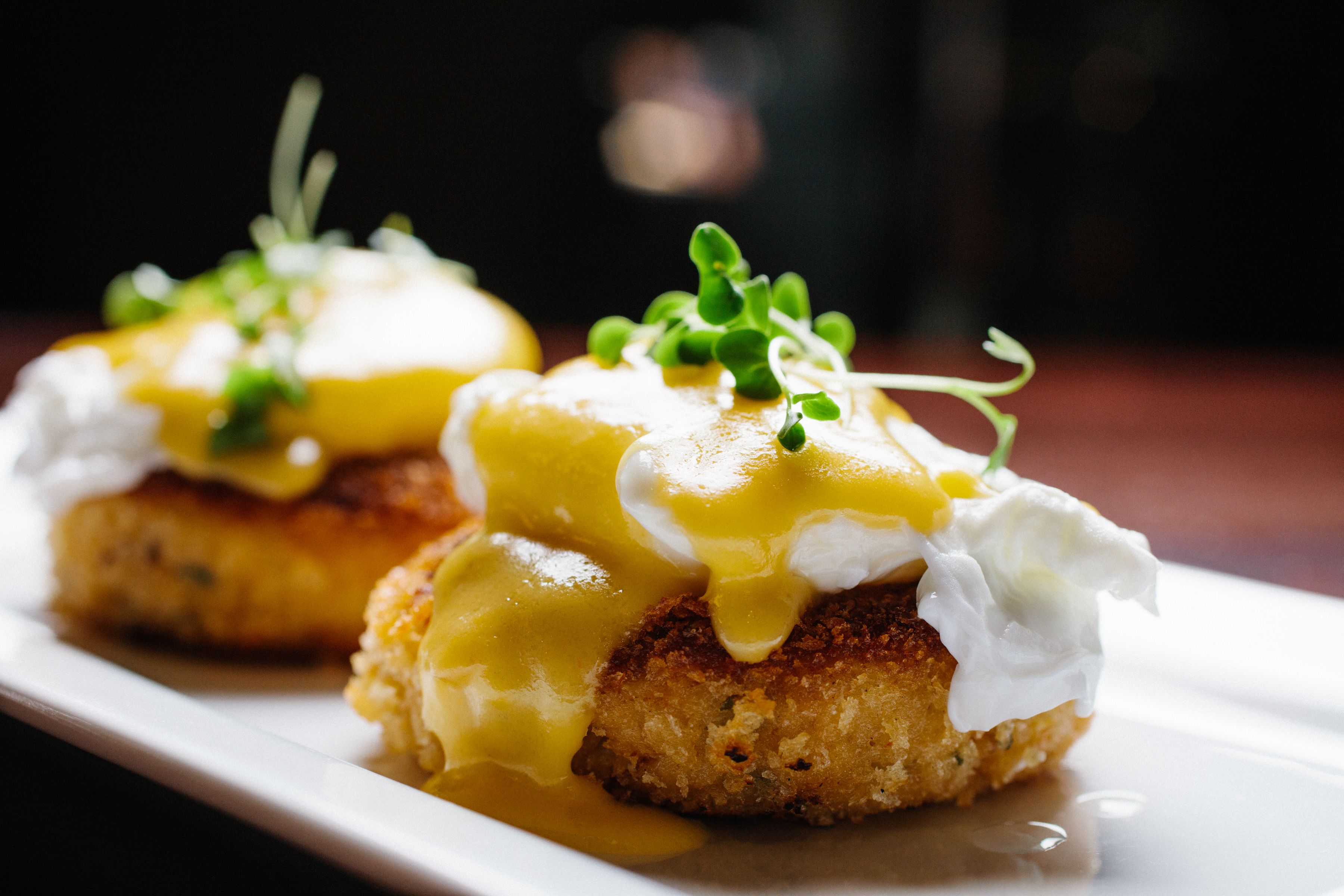 Une assiette de œufs Bén édicte nappés de sauce hollandaise et décorée d’herbes vertes, le tout présenté sur une assiette blanche.