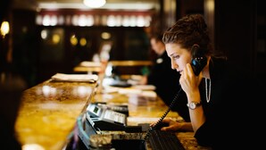 Una persona en un mostrador con un teléfono, una caja registradora y una computadora.