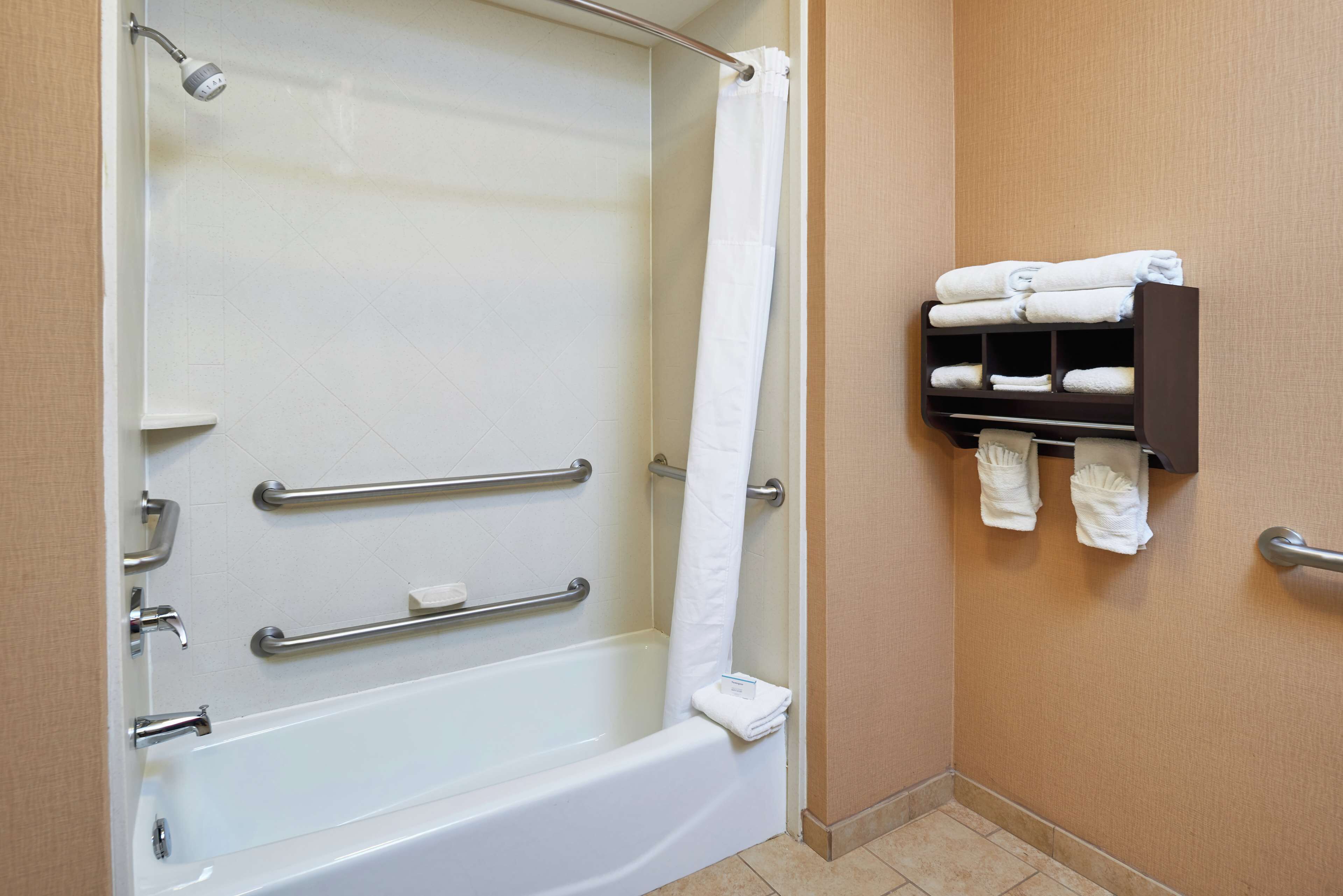 Un bagno con vasca, maniglie di sostegno, tenda della doccia e porta asciugamani con asciugni piegati.