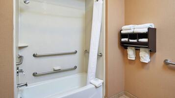 Un bagno con vasca, maniglie di sostegno, tenda della doccia e porta asciugamani con asciugni piegati.