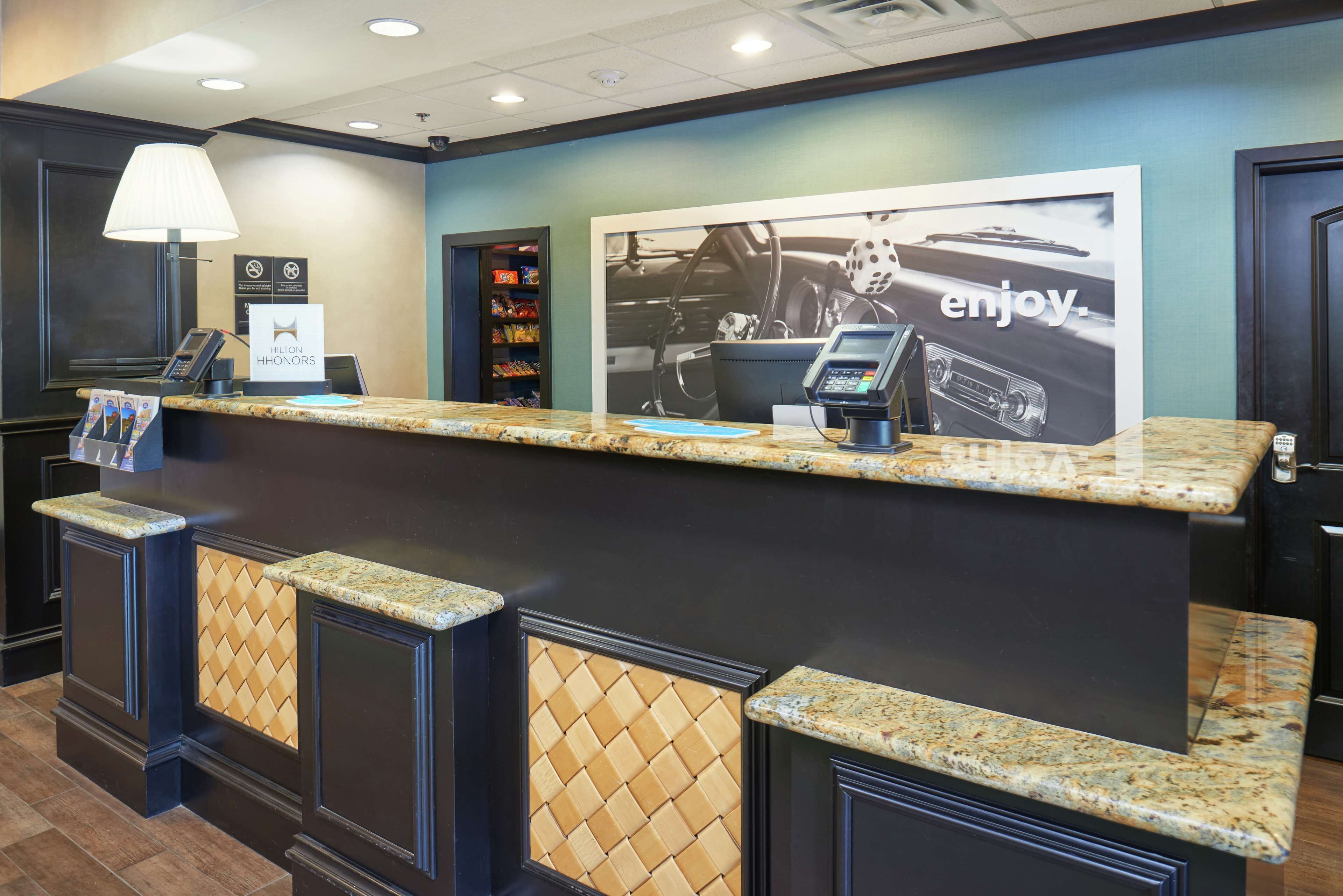 A hotel reception desk with a phone, a digital display, and a framed poster on the wall.
