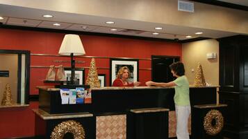 A reception desk with a red wall, a framed welcome sign, and two Christmas trees.