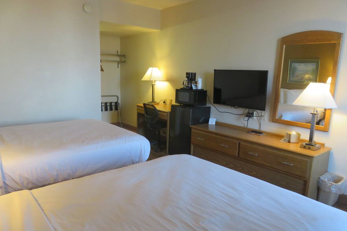 A hotel room with two beds, a desk with a computer, a television, and a mirror.