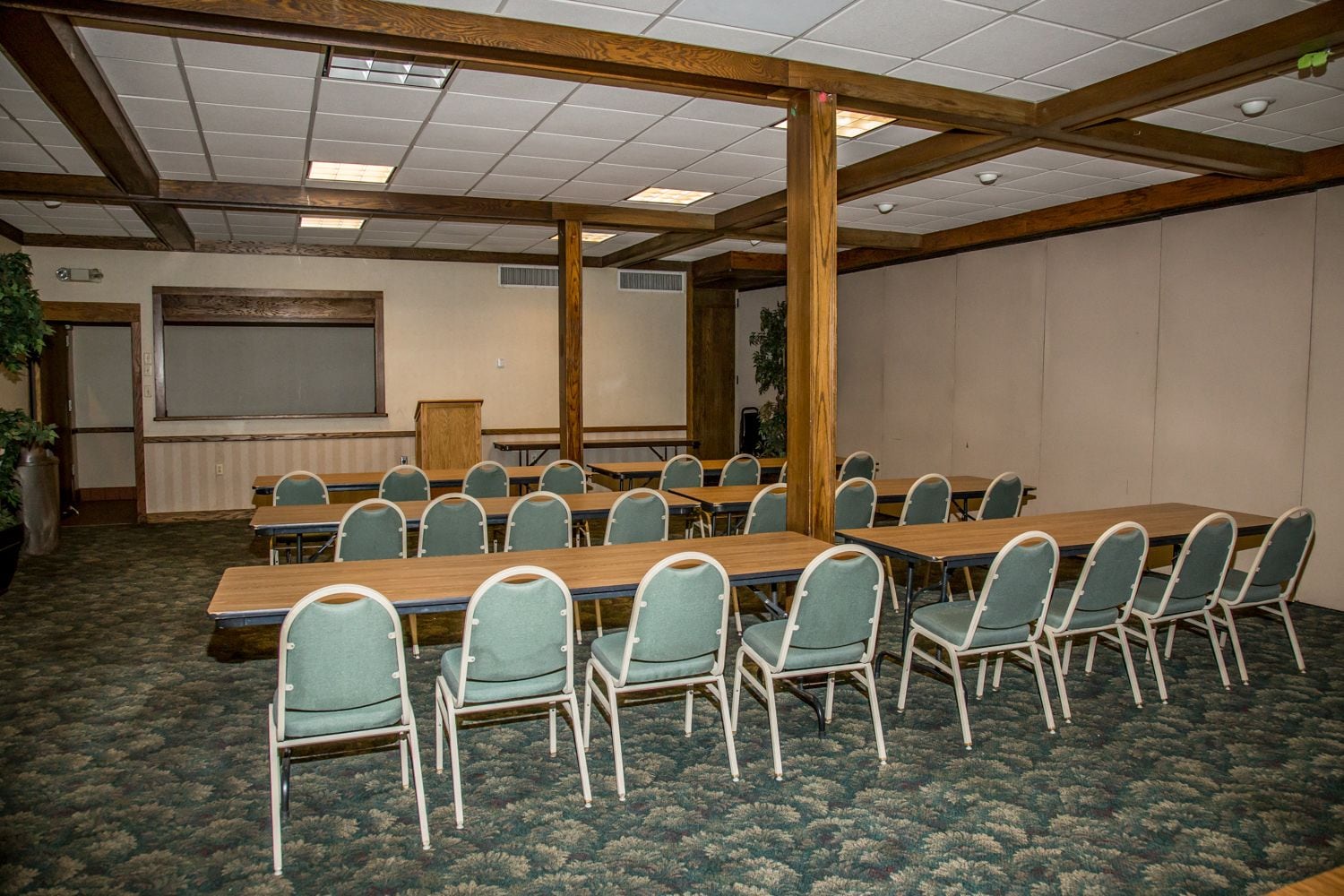 Ein Konferenzraum mit einem langen Tisch, Stühlen, Holzbalken an der Decke, Teppichboden und einer Projektionsleinwand.