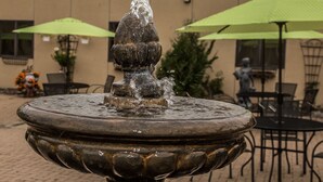 A fountain with water spouting from the top, surrounded by outdoor seating with green umbrellas. - Baymont by Wyndham Fargo (Fargo)