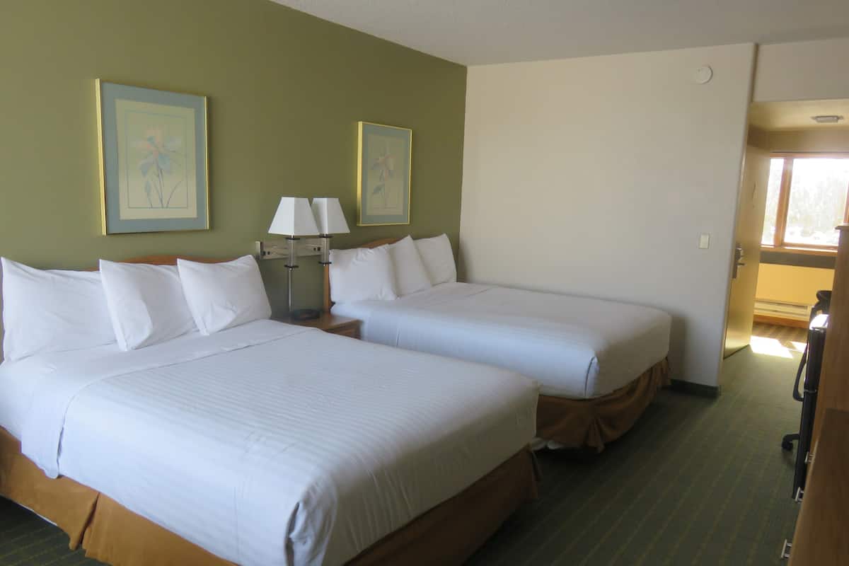 A hotel room with two beds, a nightstand with a lamp, and two framed pictures on the wall.