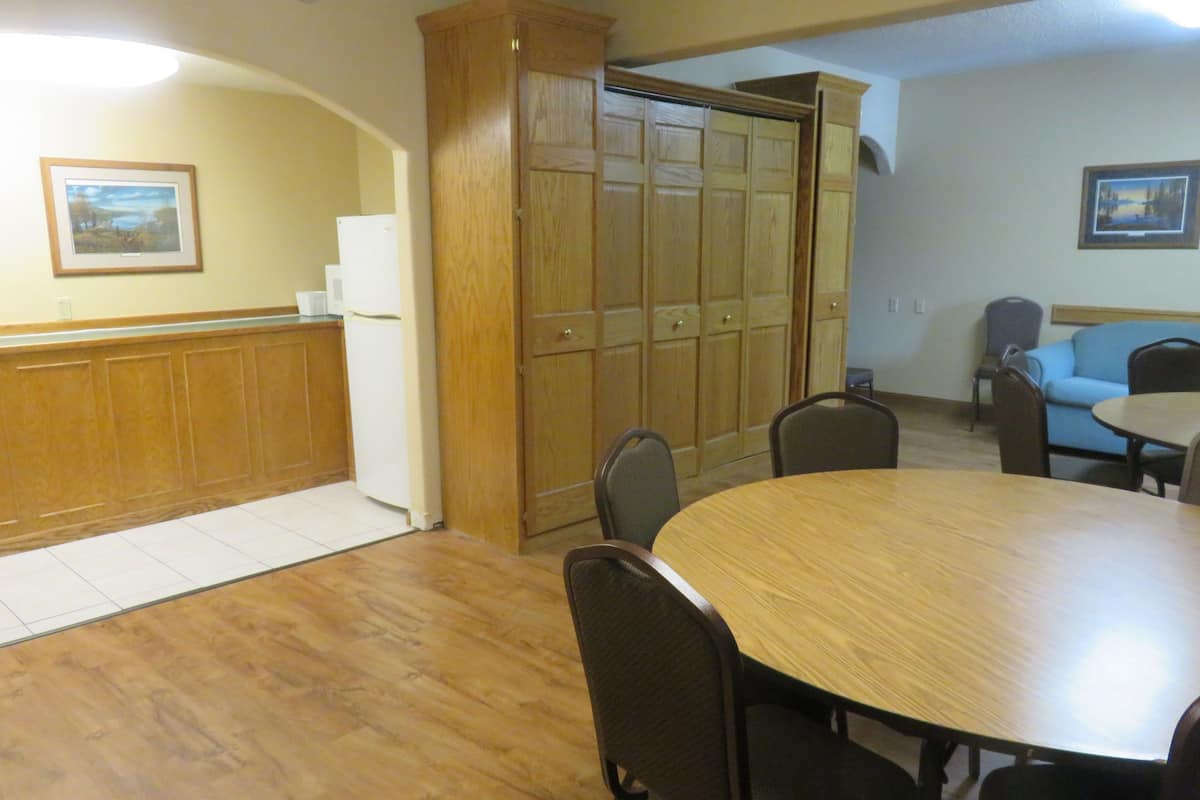 A room with a wooden table and chairs, a kitchenette, a large wooden cabinet, and a blue sofa.