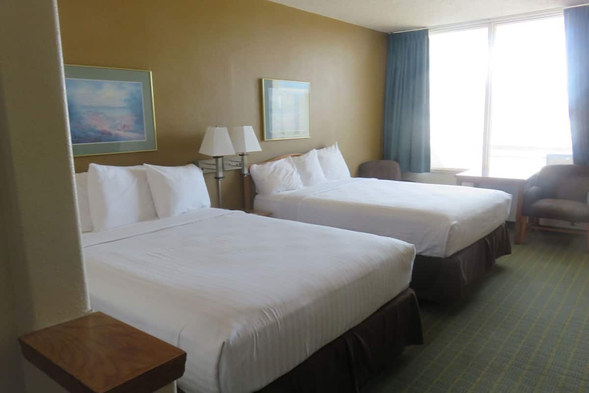 A hotel room with two beds, a desk, a chair, and a window with curtains.