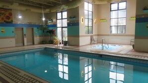An indoor swimming pool with clear water, a hot tub, and a sunlit area with chairs. - Baymont by Wyndham Fargo (Fargo)