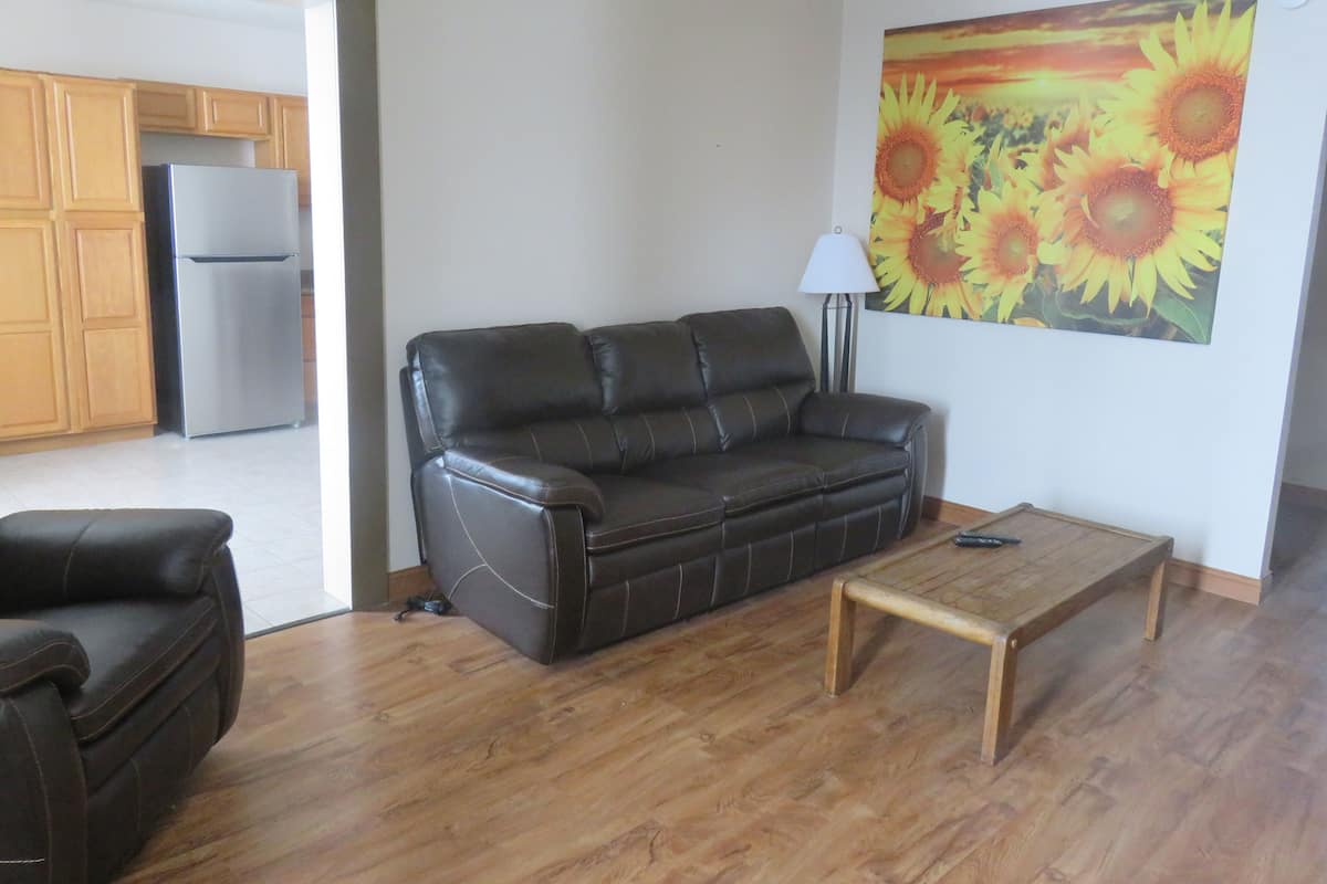 A living room with a leather sofa, a wooden coffee table, and a painting of sunflowers on the wall.
