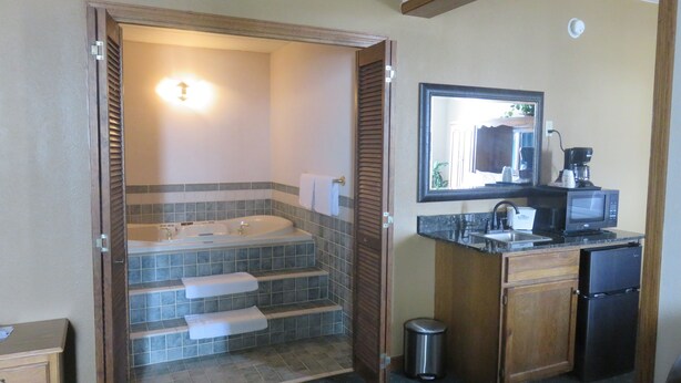 A bathroom with a bathtub, a sink, and a mirror. There is a trash can and a coffee maker on the counter. - Baymont by Wyndham Fargo (Fargo)